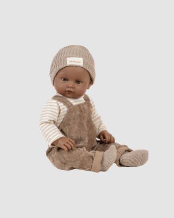 Poupon Augustin Minikane de 47 cm, sans cheveux, vêtu d’une salopette en velours milleraie châtaigne. Inclus : t-shirt rayé, bonnet taupe, chaussettes. Poupon réaliste.