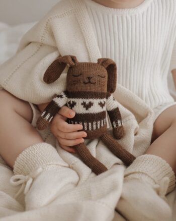 Bébé assis tenant un doudou lapin en laine baby alpaga avec pull jacquard moka, assorti à une tenue crème.