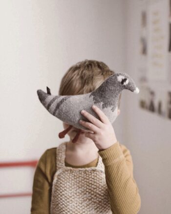 Enfant tenant un doudou pigeon Main Sauvage devant son visage.