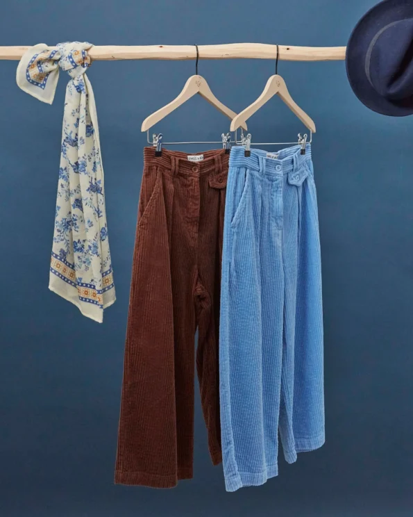 Foulard Orchid Bleu Émile et Ida suspendu à côté de deux pantalons en velours