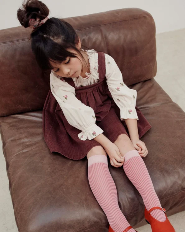 Enfant portant la blouse fleurs point de croix écru Émile et Ida avec robe salopette bordeaux