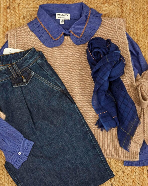 Pull sans manches à nouer beige Emile et Ida présenté à plat avec chemise bleue et pantalon en jean