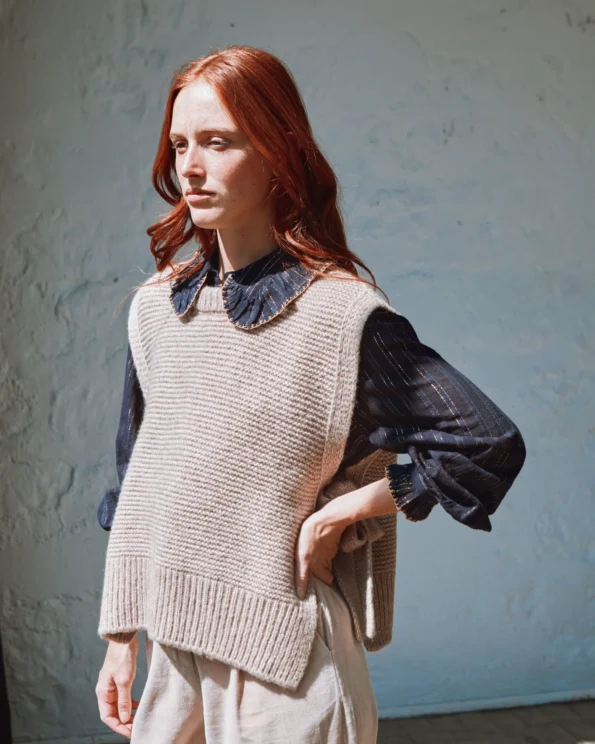 Femme de profil portant un pull sans manches à nouer beige Emile et Ida avec blouse foncée