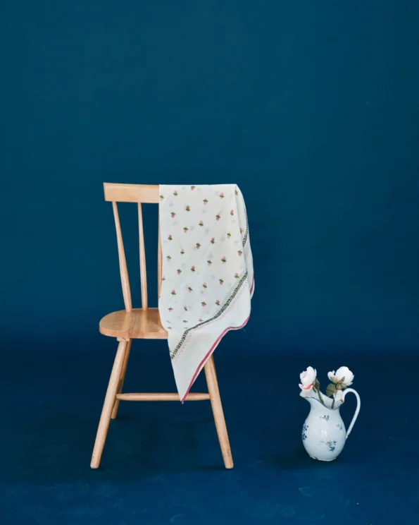 Foulard brodé roses Emile et Ida en laine écrue, posé sur une chaise en bois dans une mise en scène élégante
