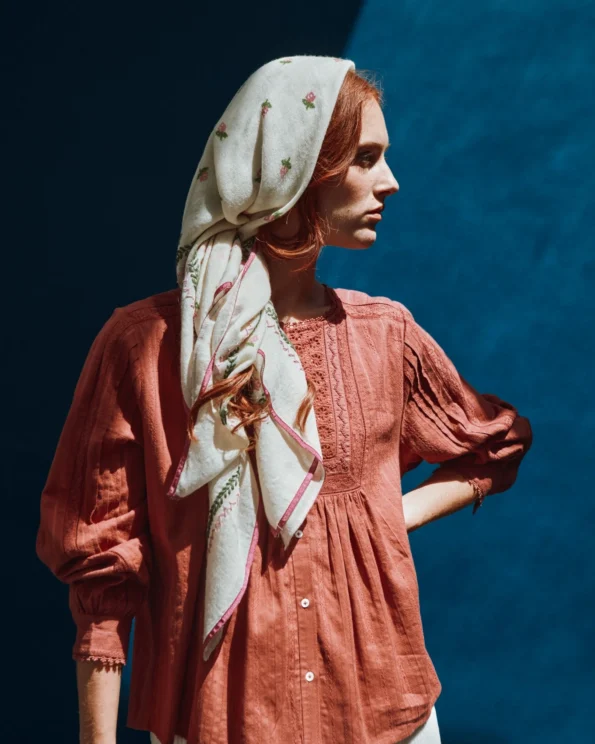 Femme portant le foulard brodé roses Emile et Ida noué sur la tête, en tenue vintage sur fond bleu
