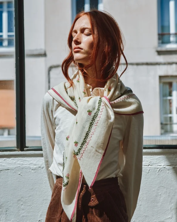 Femme portant le foulard brodé roses Emile et Ida noué autour du cou, debout près d’une fenêtre en tenue rétro