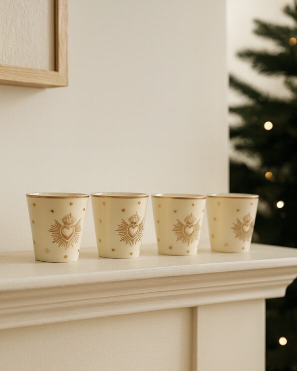 Set de 4 gobelets Ex-Voto doré Opjet Paris posés sur une cheminée, en faïence blanche décorée de cœurs dorés.