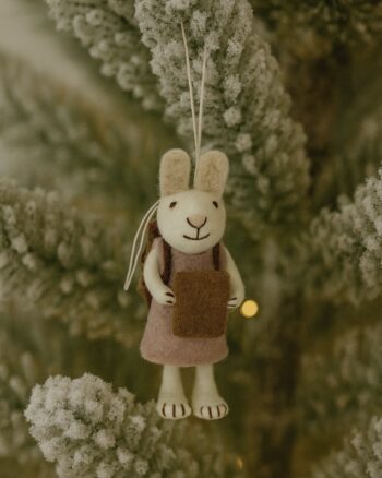 Décoration de Noël en feutre Gry & Sif représentant un lapin blanc avec une robe lavande et un petit livre, suspendu dans un sapin.