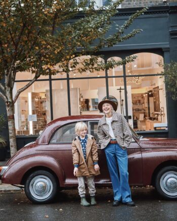 Enfant portant la parka fourrée taupe Émile et Ida, posé avec un adulte devant une voiture vintage