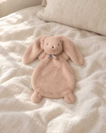 Doudou lapin Roy Pale Tuscany Liewood sur un lit beige