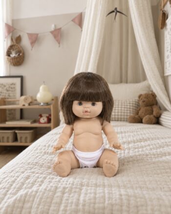 Poupée Chloé Minikane assise sur un lit dans une chambre d’enfant