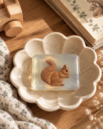 Savon écureuil Ludi Soap transparent dans une coupelle fleur en céramique beige sur fond de bois naturel.